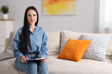 Photo of Professional psychologist with clipboard and pen on sofa in office