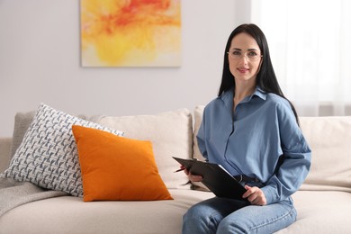 Photo of Professional psychologist with clipboard and pen on sofa in office