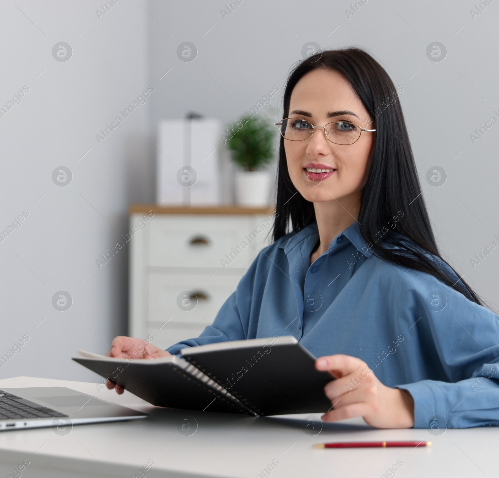 Professional psychologist with notebook and laptop at table in office Photo of Professional psychologist with notebook and laptop at table in office
