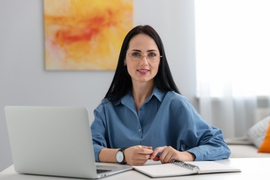 Photo of Professional psychologist with laptop, notebook and pen at table in office