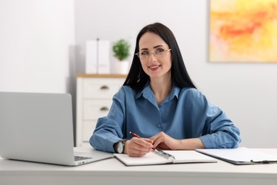 Photo of Professional psychologist with laptop, notebook and pen at table in office