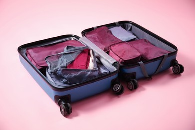 Photo of Open suitcase with packing cubes on pink background