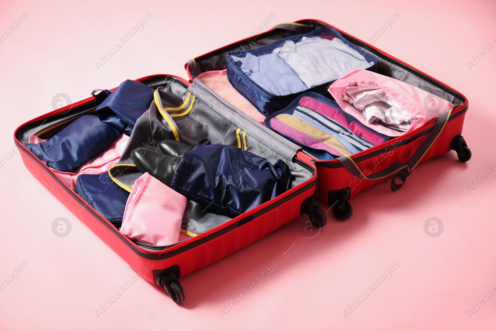 Open suitcase with packing cubes on pink background Photo of Open suitcase with packing cubes on pink background