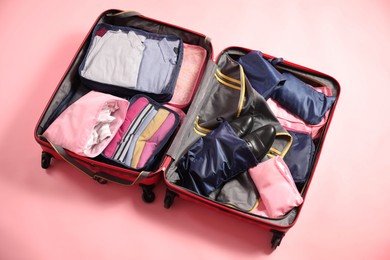 Photo of Open suitcase with packing cubes on pink background, above view