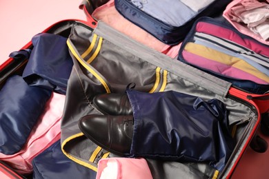 Photo of Open suitcase with packing cubes on pink background, closeup