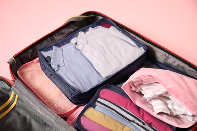 Photo of Open suitcase with packing cubes on pink background, closeup
