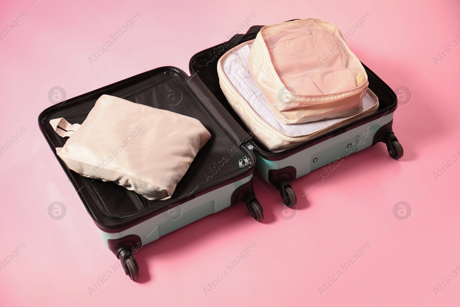 Open suitcase with packing cubes on pink background Photo of Open suitcase with packing cubes on pink background