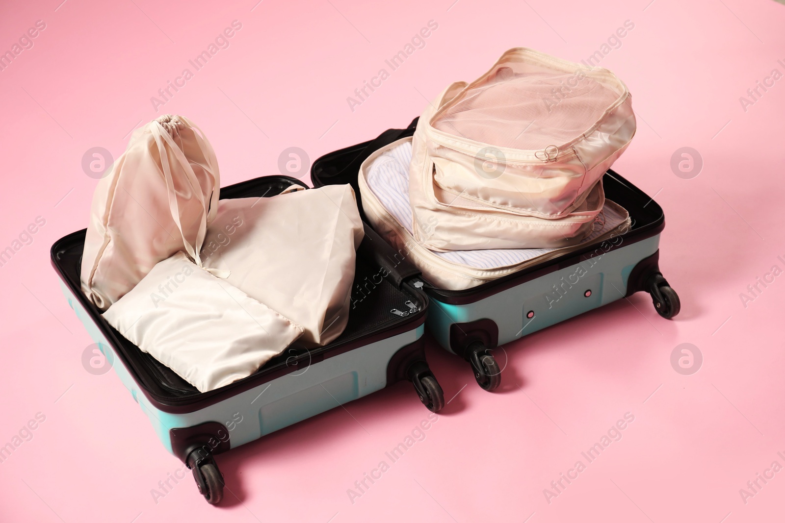 Open suitcase with packing cubes on pink background Photo of Open suitcase with packing cubes on pink background