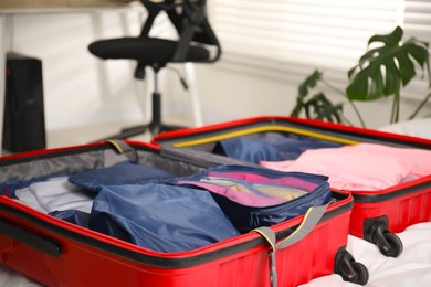 Photo of Open suitcase with packing cubes on bed indoors, closeup