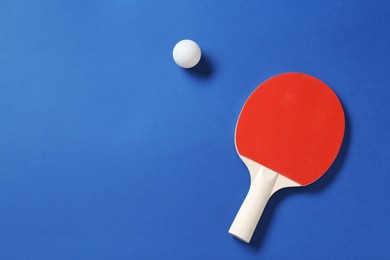 Photo of Ping pong racket and ball on blue background, top view. Space for text