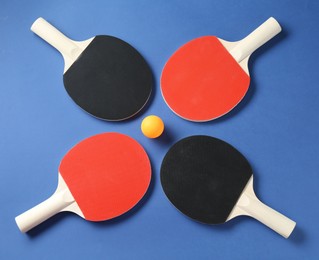 Photo of Ping pong rackets and ball on blue background, flat lay