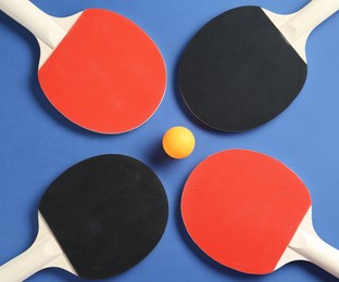 Photo of Ping pong rackets and ball on blue background, flat lay