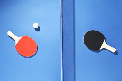 Photo of Ping pong rackets, ball and net on blue background, flat lay