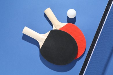 Photo of Ping pong rackets, ball and net on blue background, flat lay