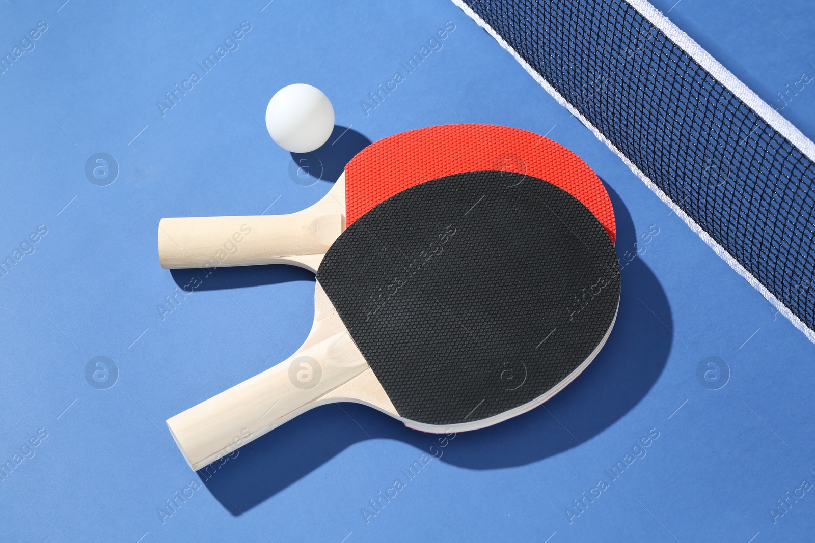 Ping pong rackets, ball and net on blue background, closeup Photo of Ping pong rackets, ball and net on blue background, closeup