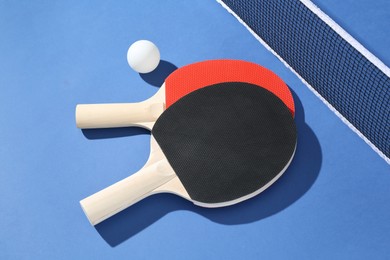 Photo of Ping pong rackets, ball and net on blue background, closeup