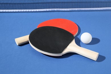 Photo of Ping pong rackets, ball and net on blue background, closeup