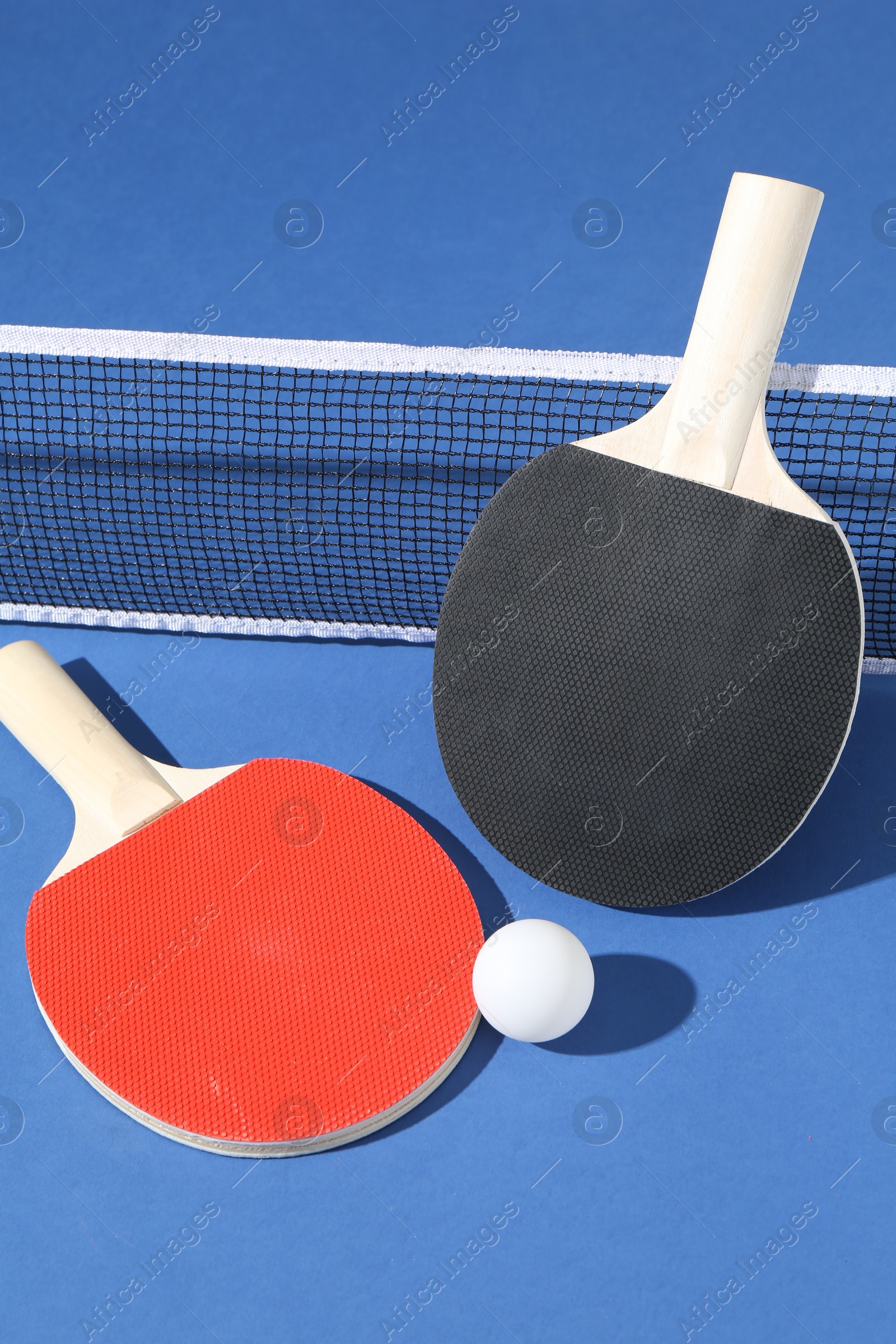 Ping pong rackets, ball and net on blue background, closeup Photo of Ping pong rackets, ball and net on blue background, closeup