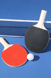 Photo of Ping pong rackets, ball and net on blue background, closeup