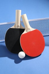 Photo of Ping pong rackets, ball and net on blue background