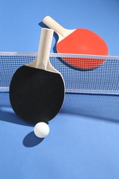 Photo of Ping pong rackets, ball and net on blue background