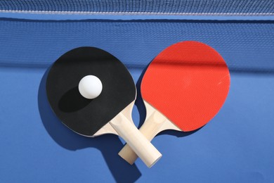 Photo of Ping pong rackets, ball and net on blue background, flat lay