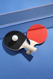 Photo of Ping pong rackets, ball and net on blue background