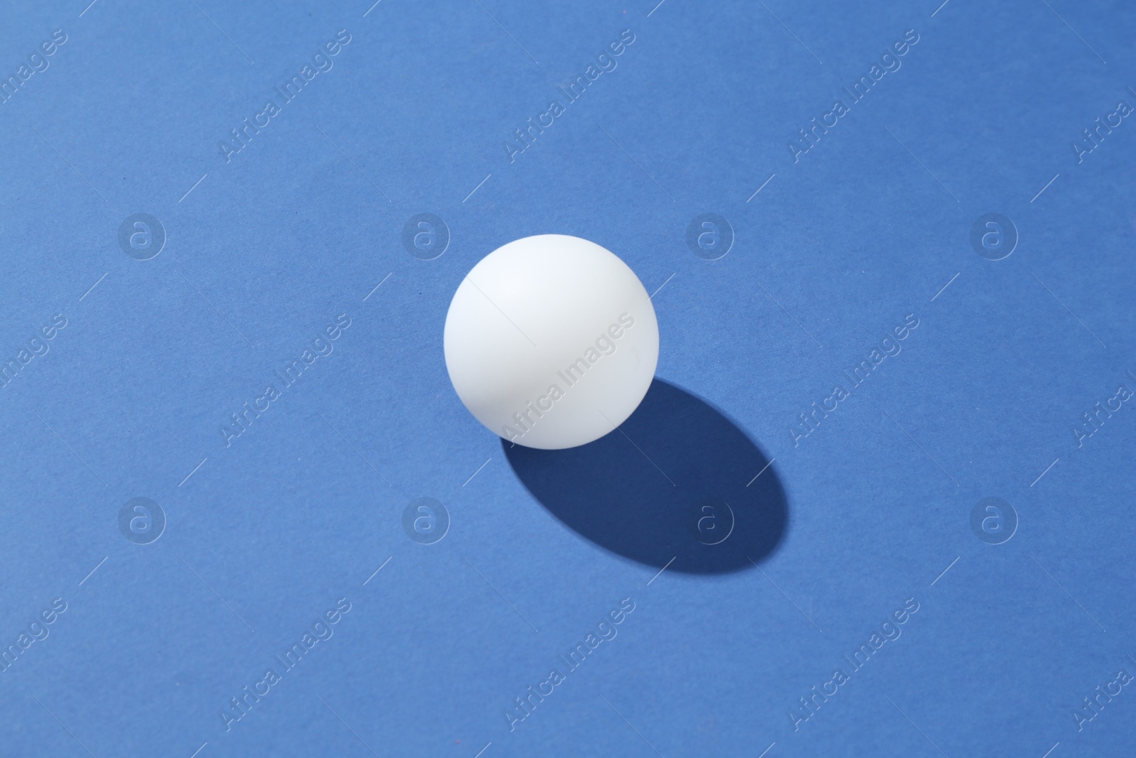 One ping pong ball on blue background Photo of One ping pong ball on blue background