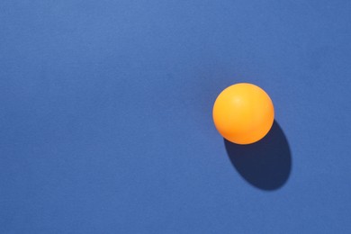 Photo of One ping pong ball on blue background, top view. Space for text