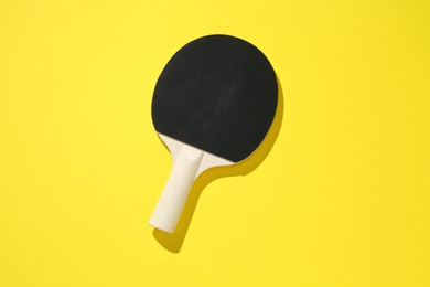 Photo of One ping pong racket on yellow background, top view
