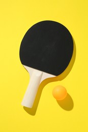 Photo of Ping pong racket and ball on yellow background, top view