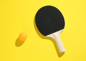 Photo of Ping pong racket and ball on yellow background, top view