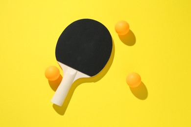 Photo of Ping pong racket and balls on yellow background, top view