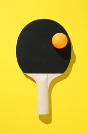 Photo of Ping pong racket and ball on yellow background, top view