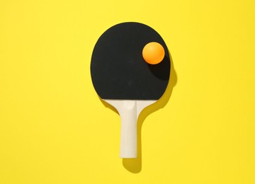 Photo of Ping pong racket and ball on yellow background, top view