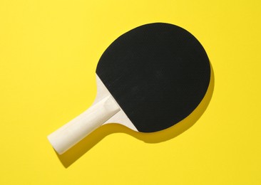 Photo of One ping pong racket on yellow background, top view