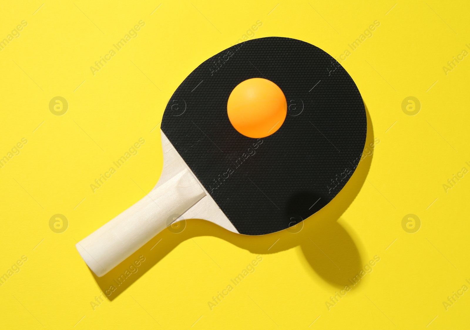 Ping pong racket and ball on yellow background, top view Photo of Ping pong racket and ball on yellow background, top view