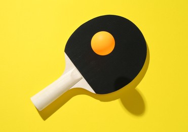 Photo of Ping pong racket and ball on yellow background, top view
