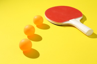Photo of Ping pong racket and balls on yellow background, closeup
