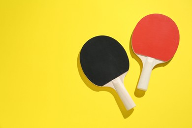 Photo of Ping pong rackets on yellow background, top view. Space for text
