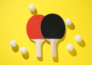Photo of Ping pong rackets and balls on yellow background, flat lay