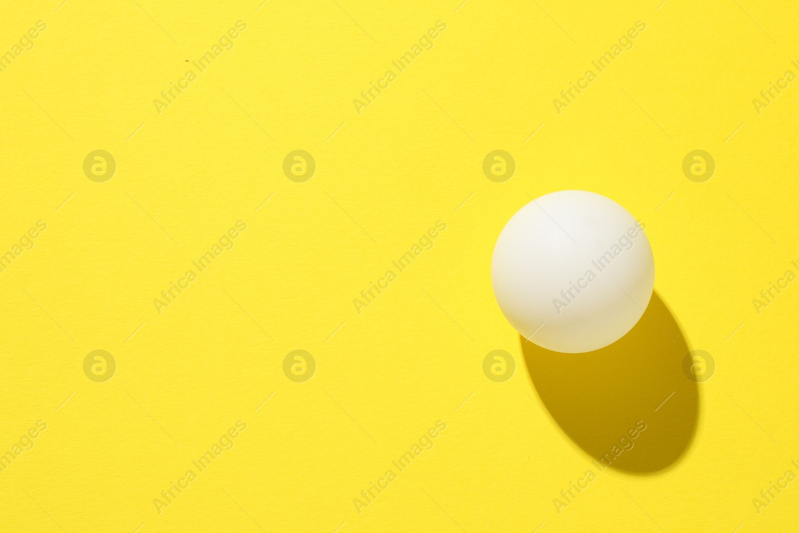 One ping pong ball on yellow background, top view. Space for text Photo of One ping pong ball on yellow background, top view. Space for text