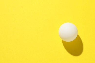 Photo of One ping pong ball on yellow background, top view. Space for text