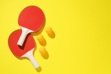 Photo of Ping pong rackets and balls on yellow background, flat lay. Space for text