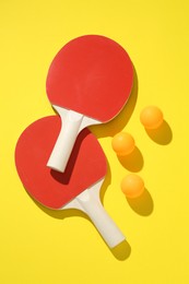 Photo of Ping pong rackets and balls on yellow background, flat lay