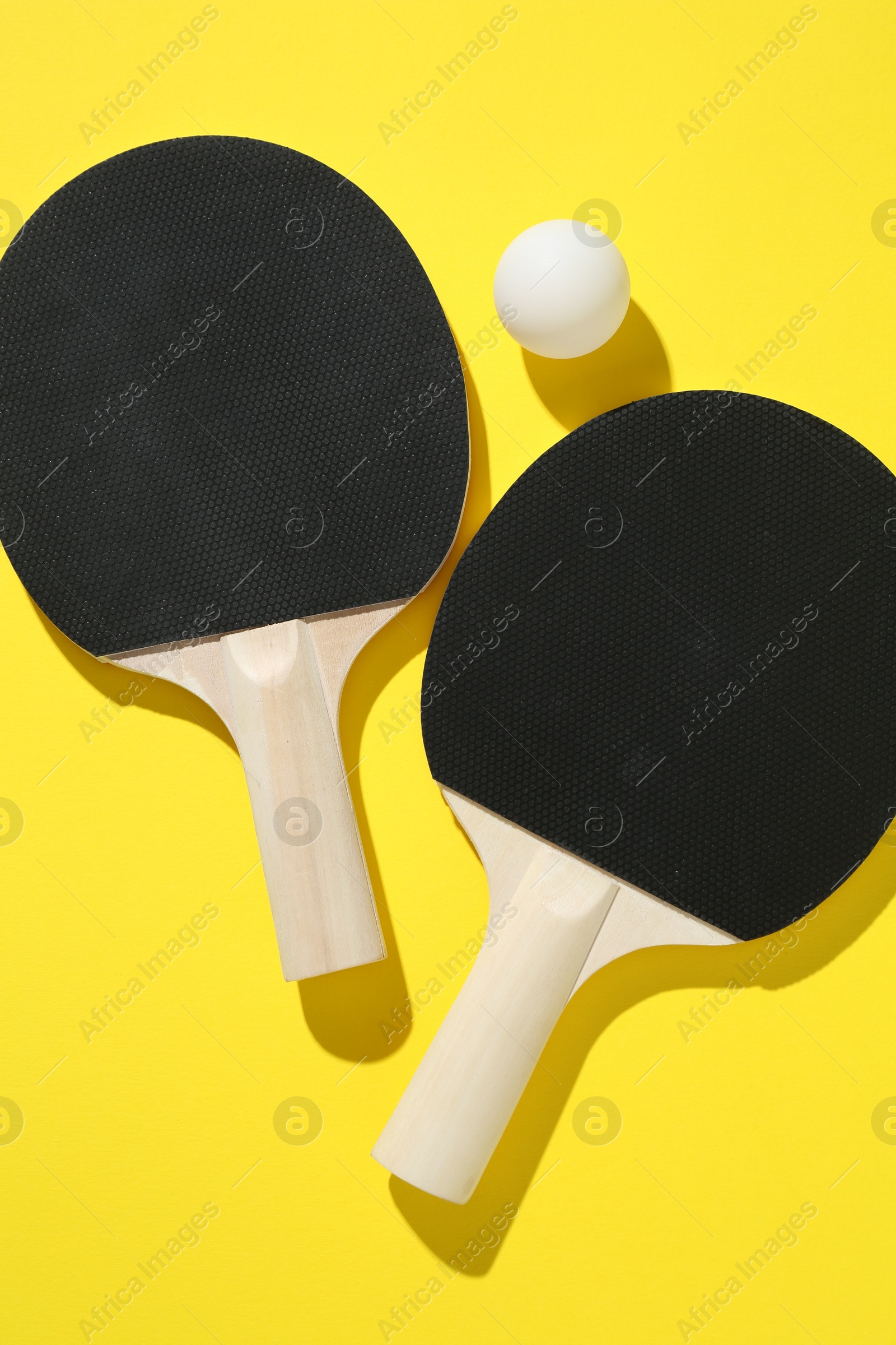 Ping pong rackets and ball on yellow background, top view Photo of Ping pong rackets and ball on yellow background, top view