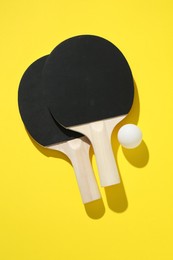Photo of Ping pong rackets and ball on yellow background, top view