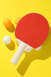 Photo of Ping pong racket and balls on yellow background, top view