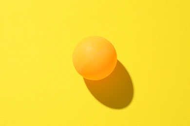Photo of One ping pong ball on yellow background, top view