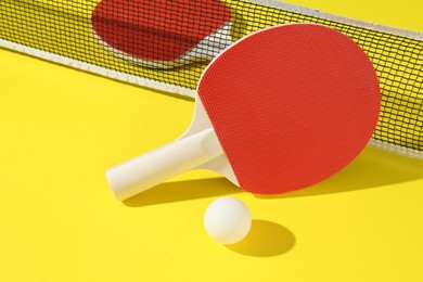 Photo of Ping pong rackets, ball and net on yellow background, closeup